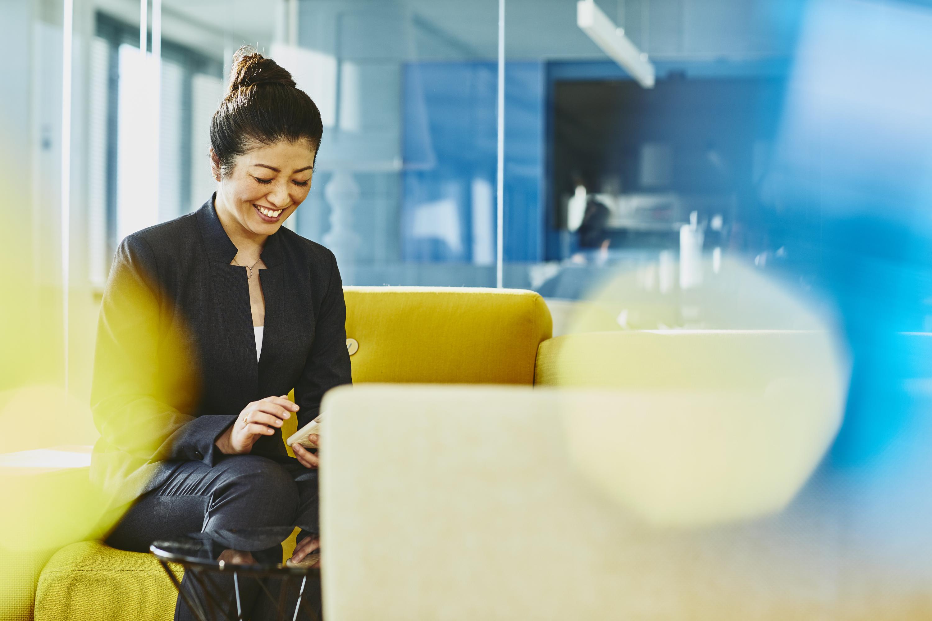 Woman looking at her cell phone smiling. Japan. Primary color: yellow.