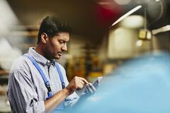 Blue-collar worker from India typing on his smartphone. Tech environment. Factory. Primary color blue. Secondary color red.