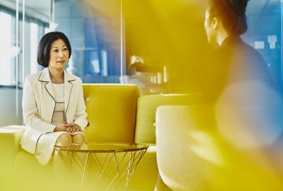 Women in an office talking. Japan. Primary color: yellow.